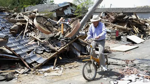 A man on a bicycle next to the rubble of a collapsed house in