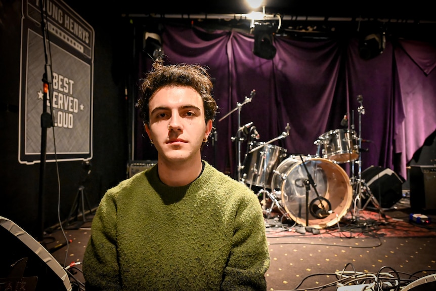 A young man wearing a green jumper in a performance venue.