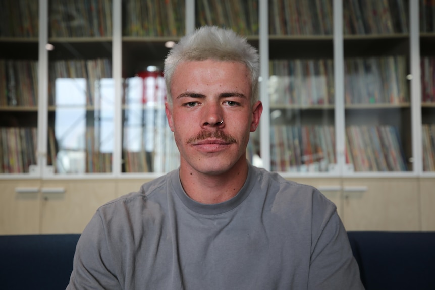A young man with bleached hair and a nose ring sits in an office.