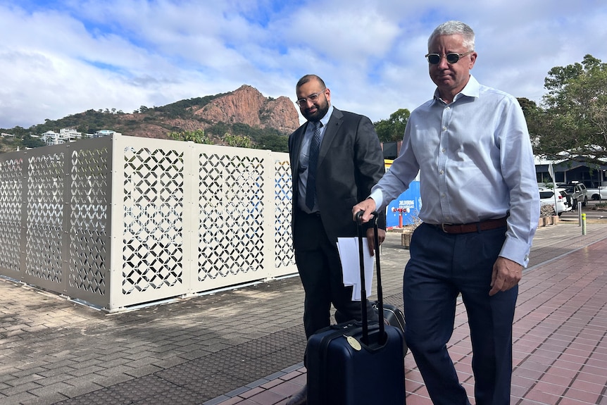 two men walking down path dressed in work clothes in front of mountain