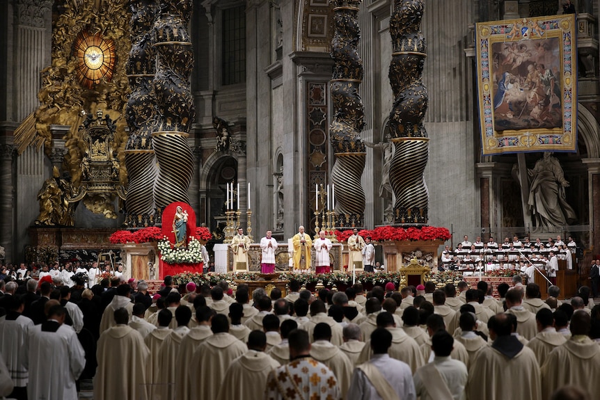 A large group of people dressed in white stand at a service inside a large church
