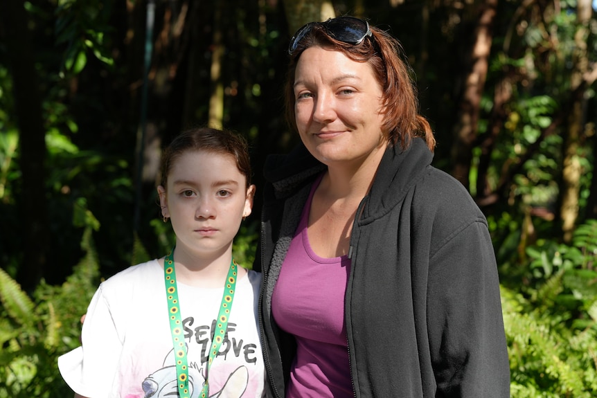A girl stands next to a woman and they both look serious.