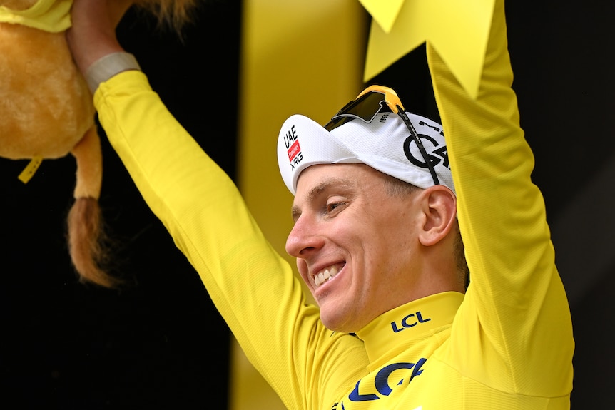 Tadej Pogačar holds up his hands in yellow