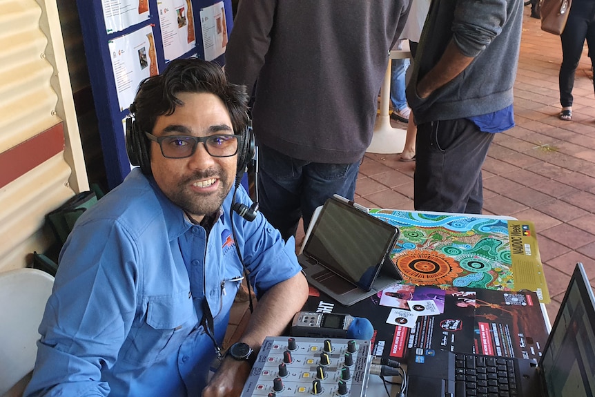 Matt with a headset and glasses on in front of radio broadcast equipment.