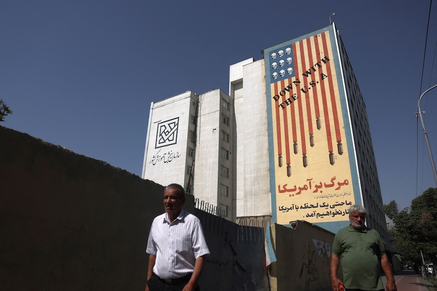A man walks next to a mural with a bloodied US flag.