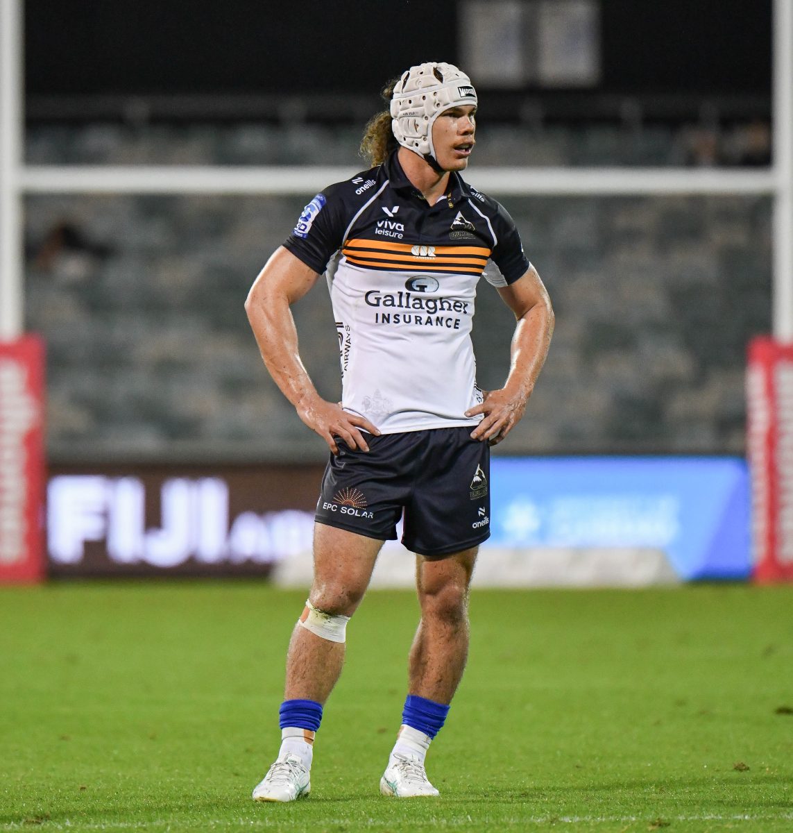 Brumbies player Kye Oats standing on the field at GIO Stadium with goal posts and empty seats behind him.