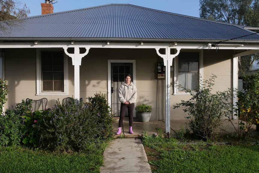 woman in a tracksuit and gum boots stands in front of a house
