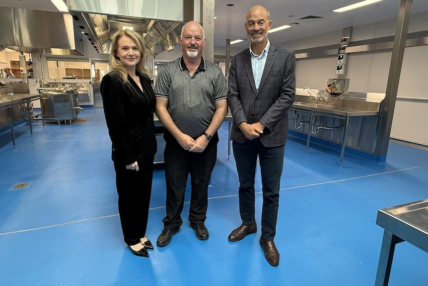 Three people pose for a photo in a prison kitchen.