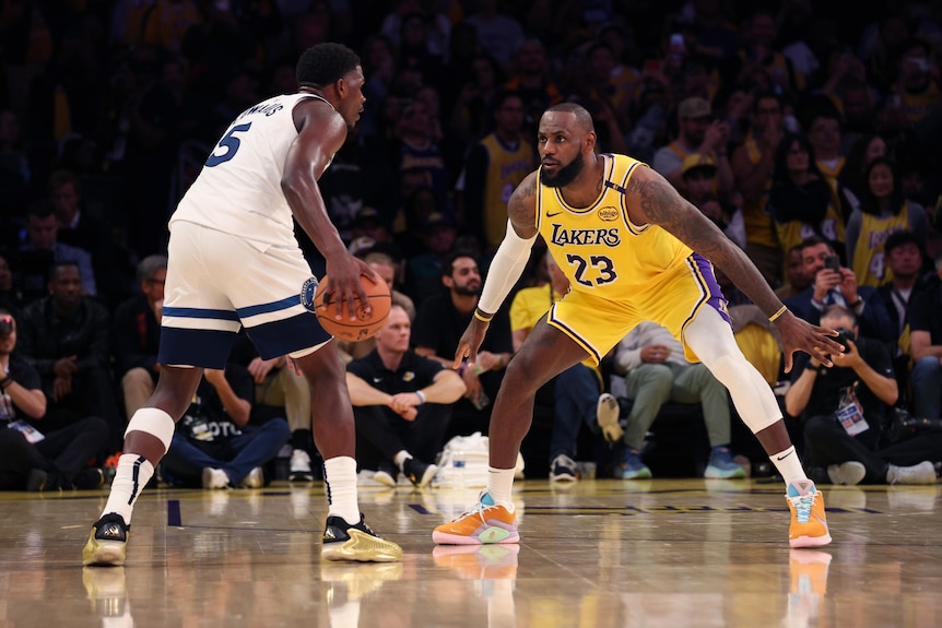 Anthony Edwards holds basketball in right hand while LeBron James defends.