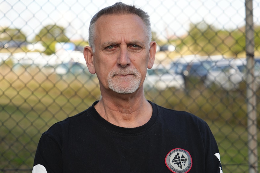 Stuart Edward looks straight ahead, a wire fence is behind him.