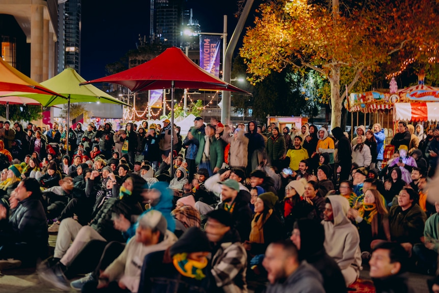 A group of people, some in Australian jerseys, at outdoor night-time viewing party