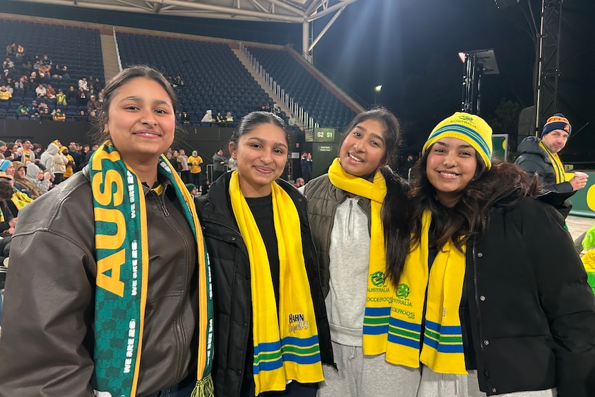 A group of four South Asian female football fans wearing Socceroos gear at outdoor viewing party