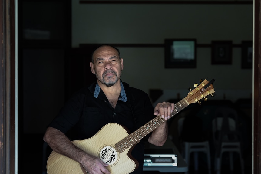 Jason holding guitar staring into camera.