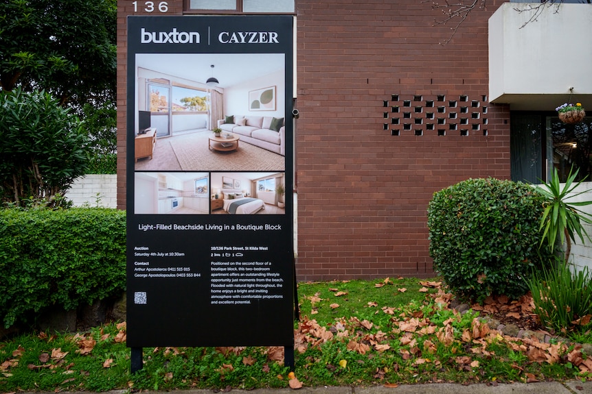 A large sign stands outside a multi-storey brown brick building with real estate information including an auction date.