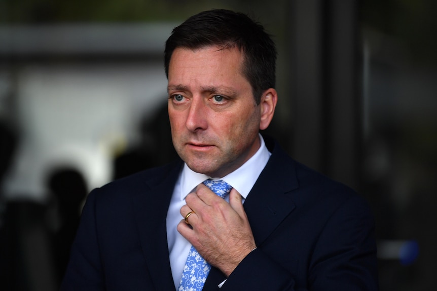 A profile shot of a man wearing a suit holding onto his tie knot.