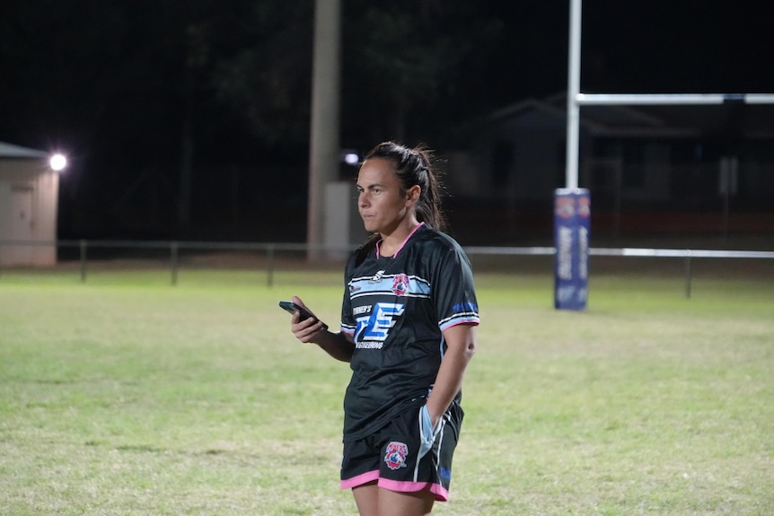 Coach holding phone in hand watching on football field, night time