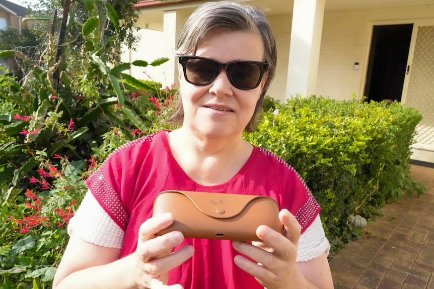 A woman wearing meta glasses and a red shirt holds meta glasses case