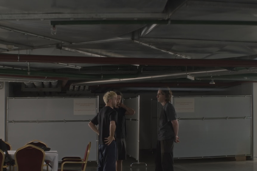 Three men stand in a dimly lit room.