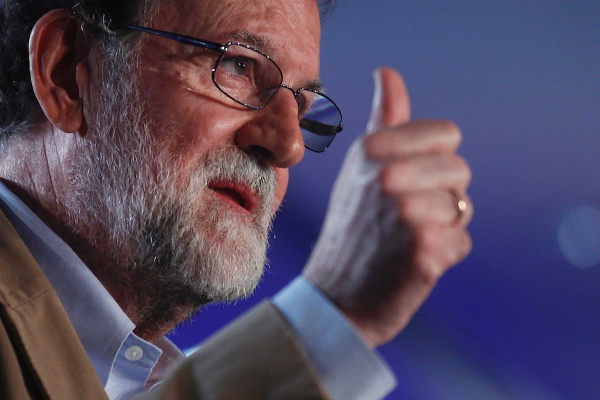 Spain's Prime Minister Mariano Rajoy holds his thumb up. He's middle aged and wearing glasses