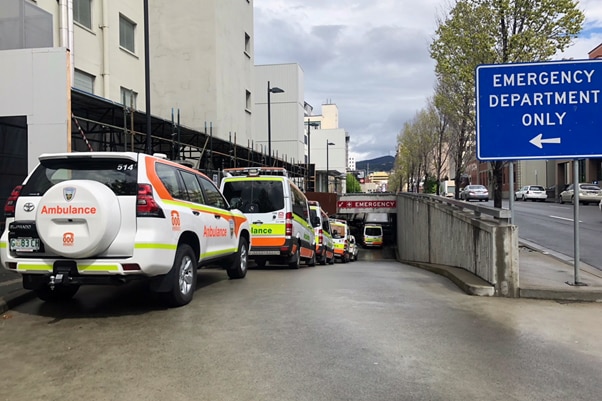 Ambulances line up on a ramp driveway beside an emergency department entrance sign.