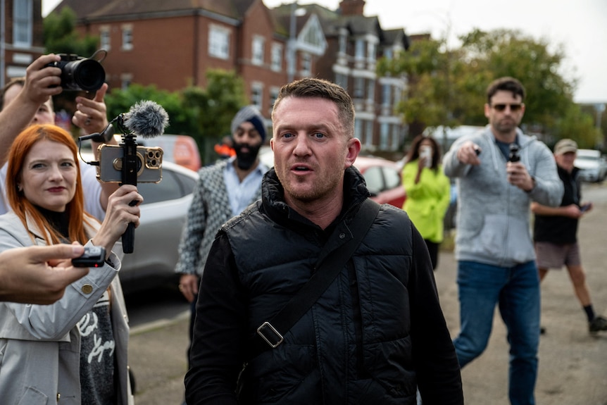 Tommy Robinson arriving at a police station with supporters and media around him.