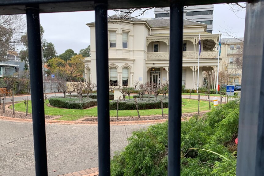 An old two-storey building seen through the metal bars of a fence.
