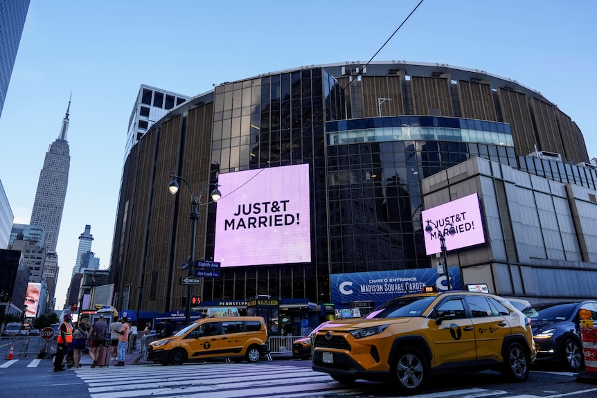 Yellow cabs drive by Madison Square Garden where two pink billboards say Just Married!