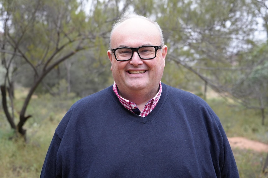 Man in blue jumper and glasses standing in green background