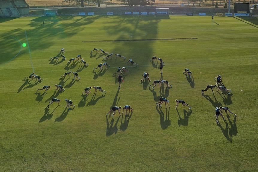 a drone shot in the air of a football team stretching in a push up position wearing green Tasmania devils shirts at sunset