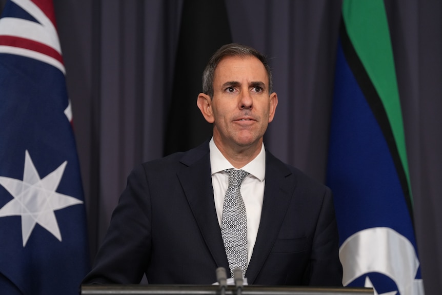 Man stands at microphone front on mid shot, press conference in blue room