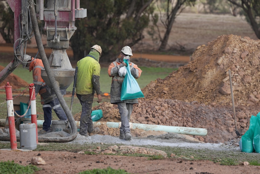 Three workers operate a mining drill rig 
