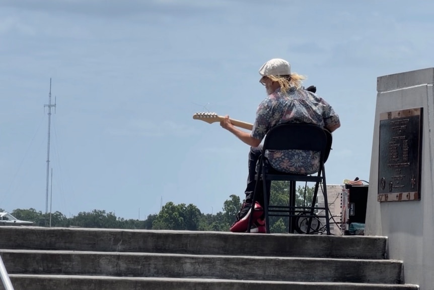 A man plays the guitar, facing away from the camera.