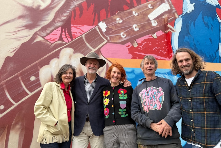 Group of people stand together in front of mural smiling