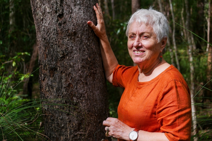A woman leaning against a tree trunk.