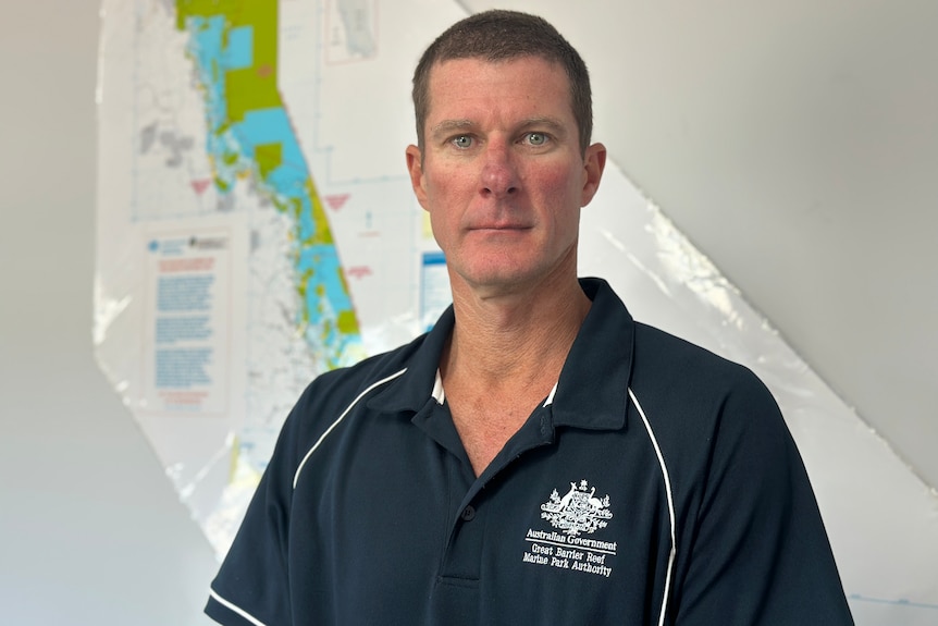 A man standing in front of a map looking at the camera with a serious expression.