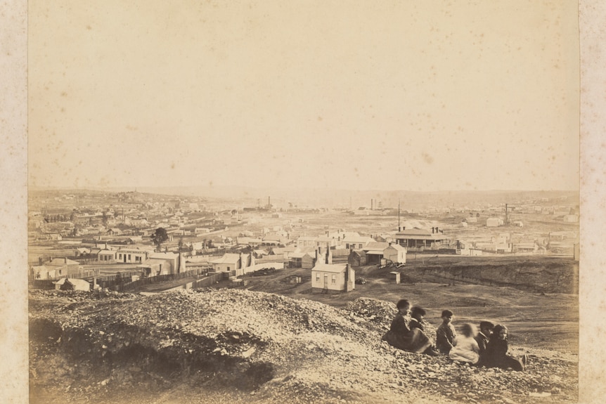 A black and white photograph of children sitting on a mullock heap on the outskirts of town.
