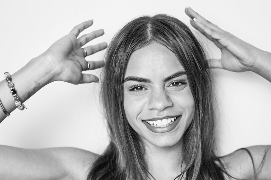 Nyima smiles, has straight hair, hands around head, but not touching, sleeveless top.