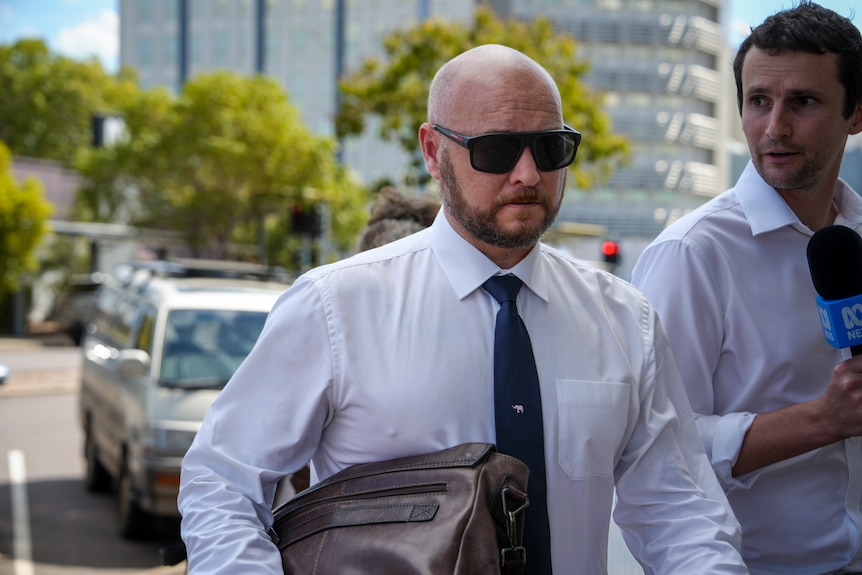 Lawyer Marty Aust walking down a footpath, towards a courthouse entrance, as a reporter follows him.