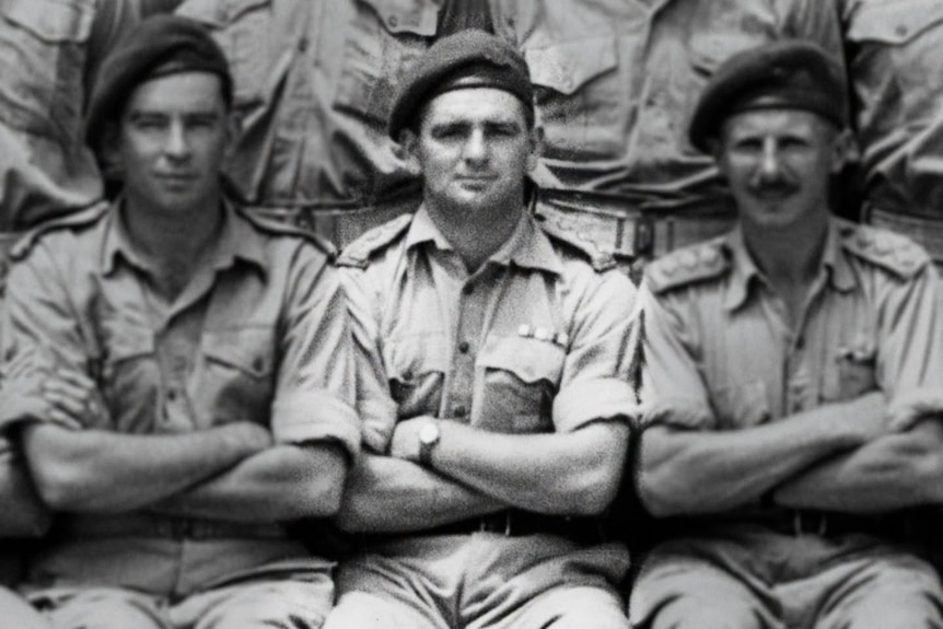 A black and white image of three men in military uniform sitting in a line with their arms crossed.