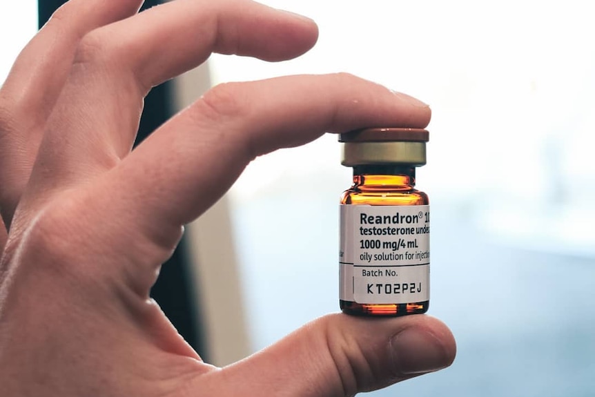 A man's hand holds a vial of testosterone medication.