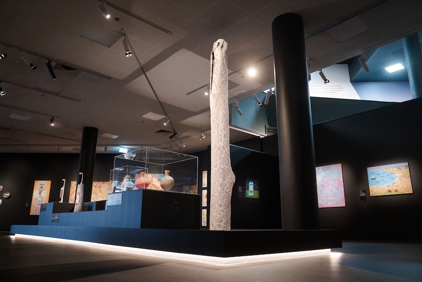 A range of artworks on display inside a gallery, including a tall wooden sculpture that has been hand-painted.