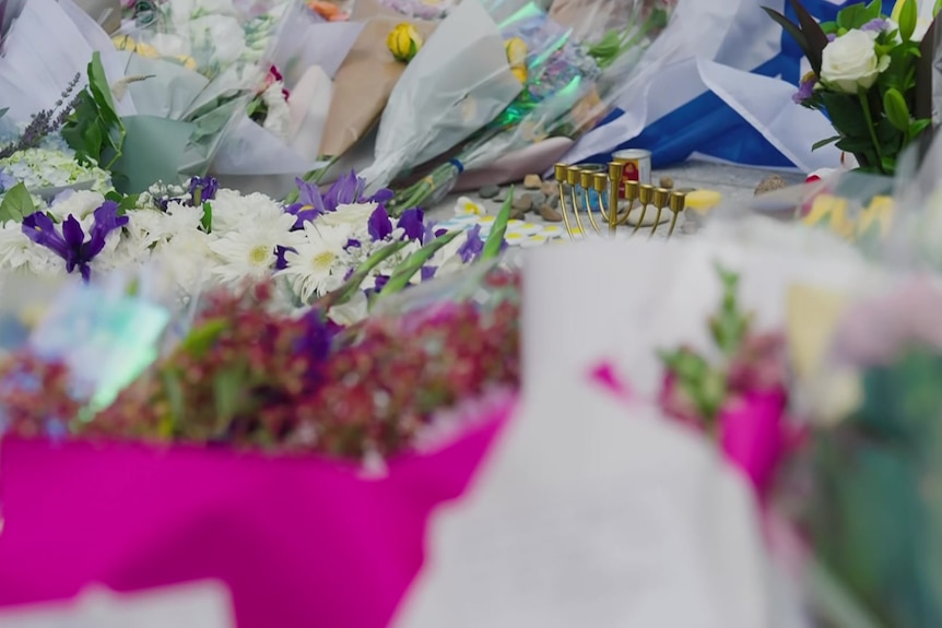 Flowers and tributes, including a menorah, laid out at vigil for Bondi attack victims.