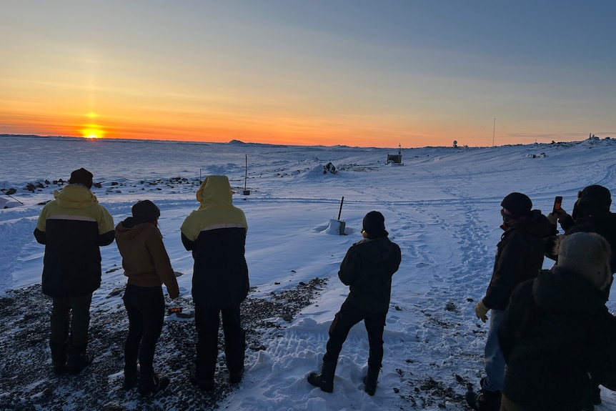 Group of people standing in the snow watching the sun rise.