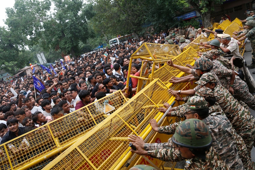 Several police officers stand behind yellow fences with a mass of people on the other side