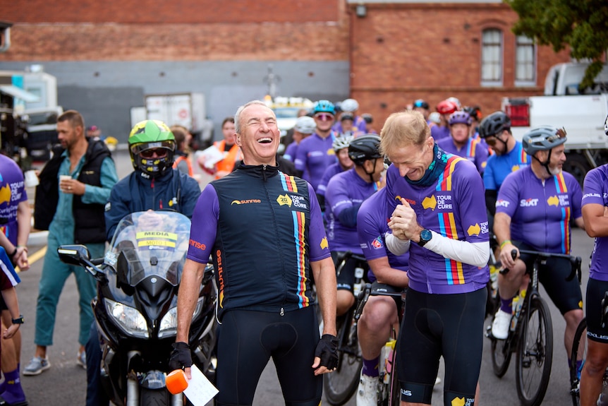 Mark Beretta and Richard Scolyer smiling and laughing, with fellow bike riders in lyra behind them.