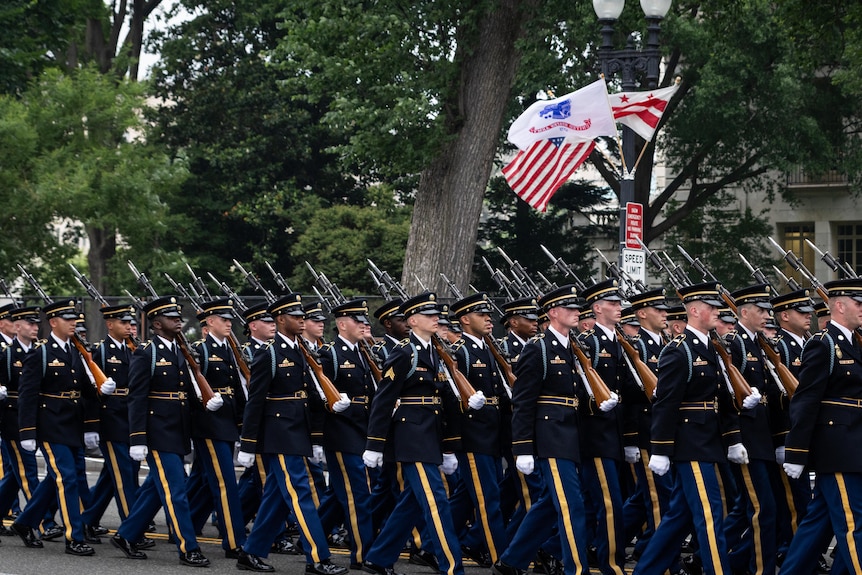 US soldiers in formal uniform march down an avenue.