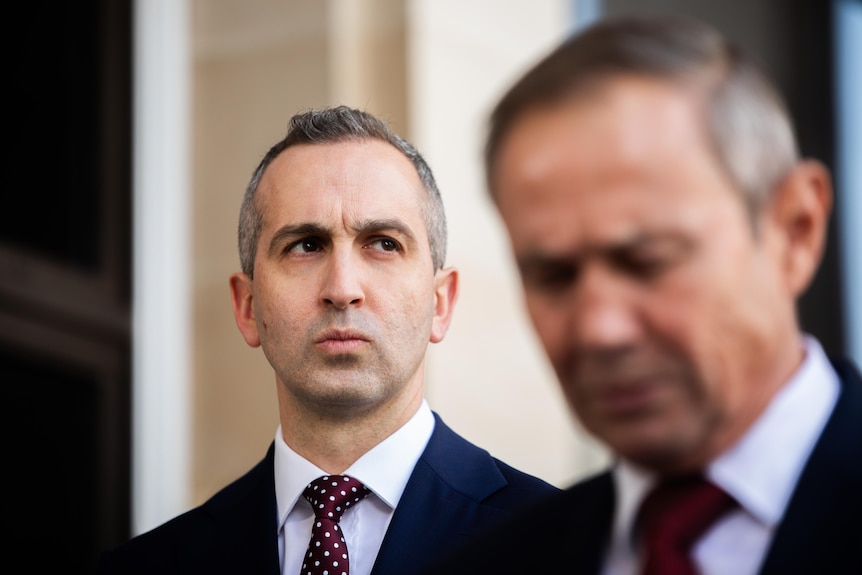 Two men listen to each other speak at a press conference.