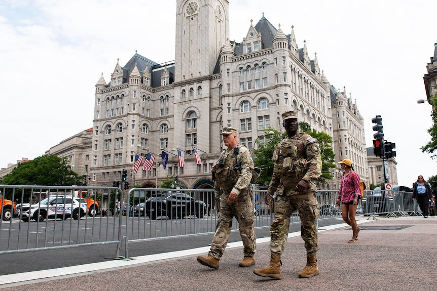 Soldiers walk on a cordoned-off footpath near a grand multi-storey building in a city.