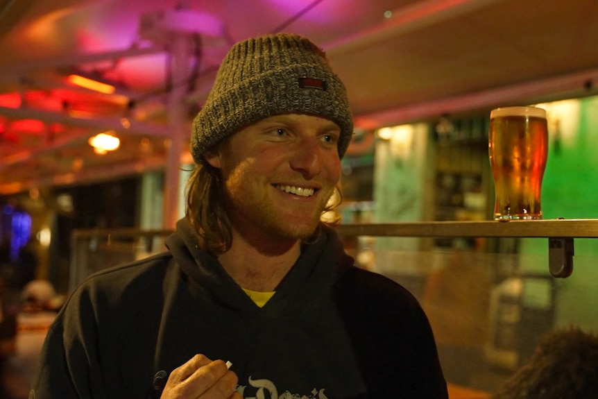 Man standing in front of a pub smoking area with beer perched up next to him