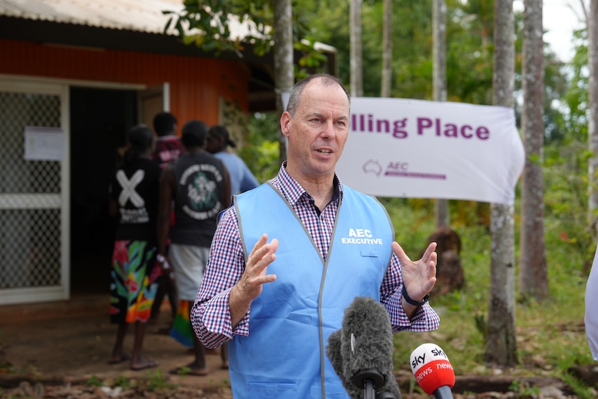 A man in a vest with the AEC logo, standing outside a building in a remote community.